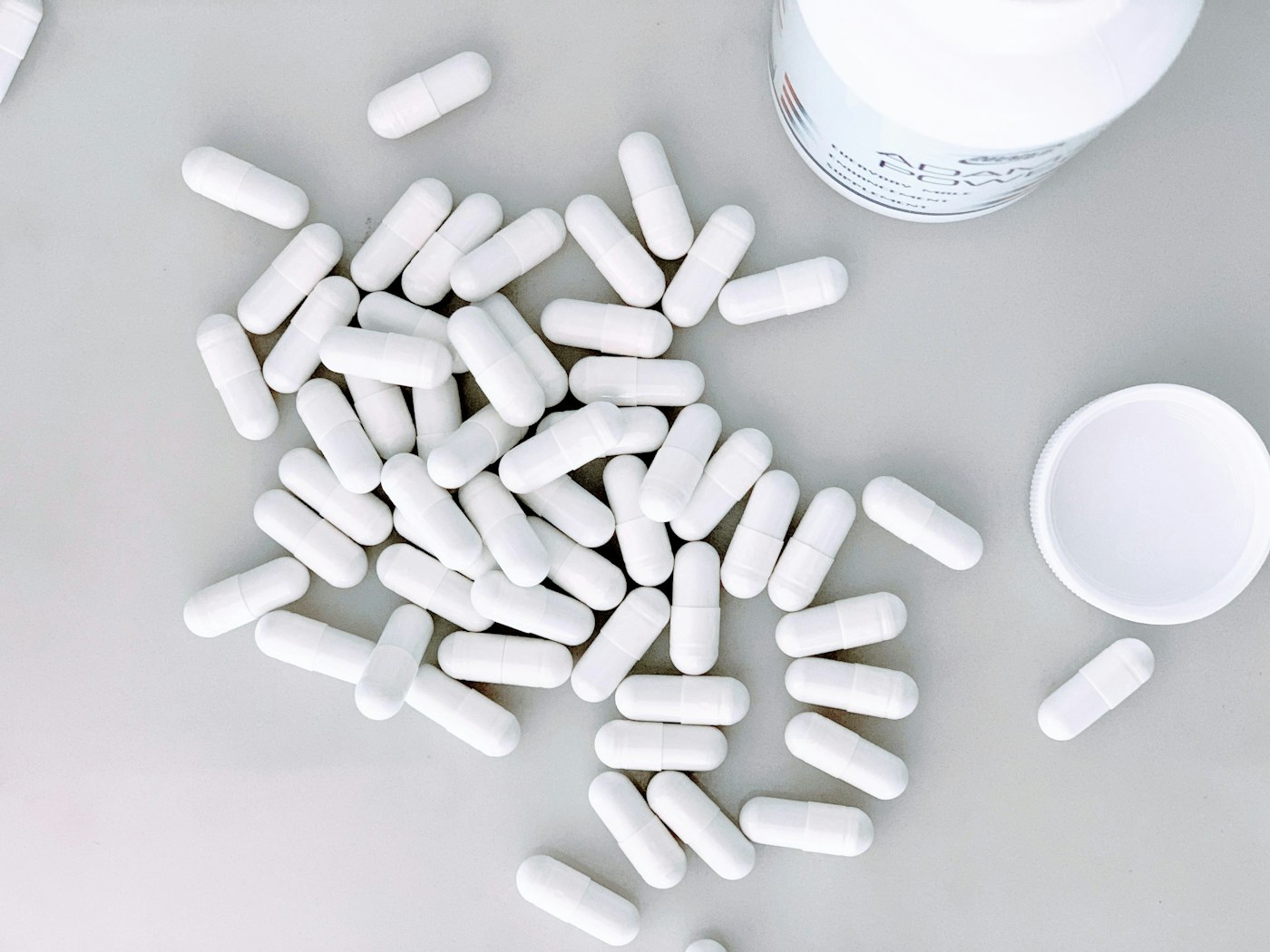 White pharmaceutical capsules beside an open container